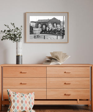 Derry Girls mural with school-uniform portraits beside a low stone wall, monochrome photograph.