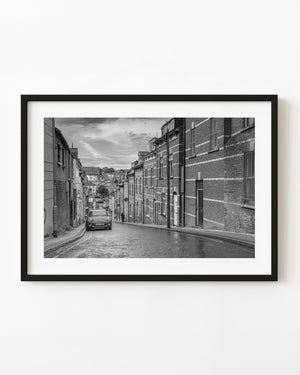 Sloping Derry street between brick facades, black and white architectural photograph.