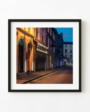 Warmly lit Derry doorways beneath a blue evening sky, colour architectural photograph.