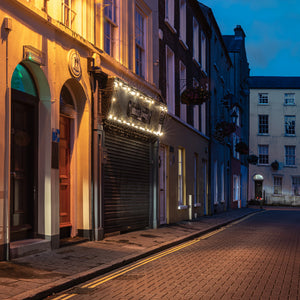 Derry street at blue hour with golden light on doors and closed shutters.
