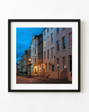 Derry townhouses with warm doorway light beneath a deep blue evening sky.