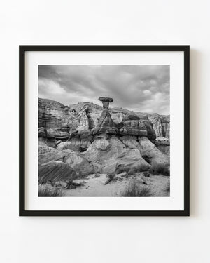 Desert hoodoo with a broad capstone beneath clouds, black and white landscape photograph.