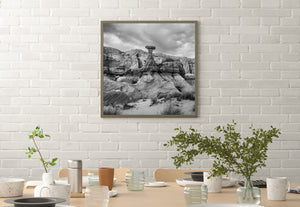 Square black and white desert scene with a capstone formation and layered rock.