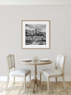 Cloudy sky above a solitary hoodoo and curved desert terrain, monochrome photograph.