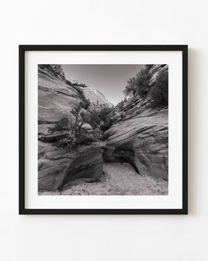 Sloping desert rock layers around a sandy passage, black and white landscape photograph.