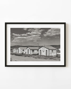 Weathered wooden cabins beside an empty road in Currie, Nevada, monochrome photograph.