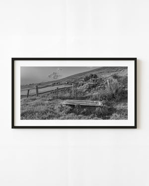 Old bathtub in a Dingle Peninsula field beside stone boundaries, black and white photograph.