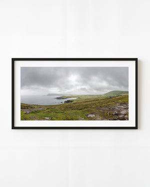 Green Dingle Peninsula coastline curving around a pale bay beneath grey clouds.