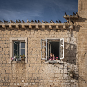 Dubrovnik stone facade with a woman at an open window and a cat nearby