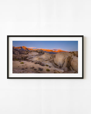 Eastern Sierra peaks glowing orange at sunrise above rounded desert boulders