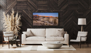 Orange sunrise illuminating distant mountains above pale desert boulders