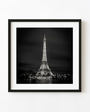 Illuminated Eiffel Tower across the dark Seine in a square black and white night photograph