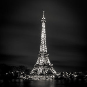 Paris night view of the Eiffel Tower with riverbank lights reflected in the Seine