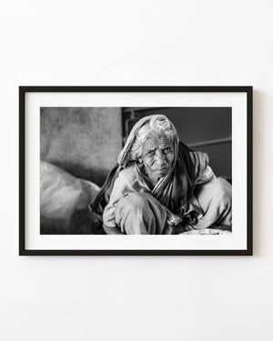 Black and white portrait of an elderly Indian woman seated low with a cloth around her head.