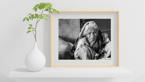 Black and white Indian portrait showing an older woman resting beside a wall.