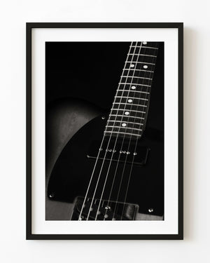 Electric guitar strings and frets emerging from shadow in black and white.