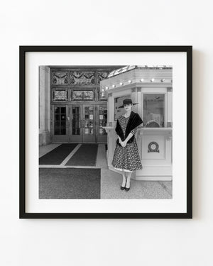 Woman in a dark hat and floral dress beside the box office at Toronto’s Elgin Theatre.