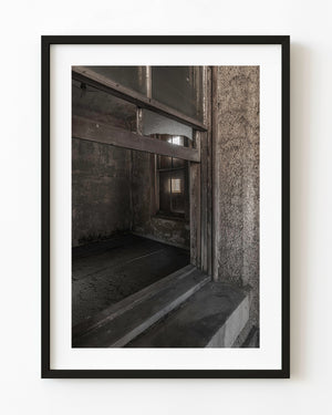 Broken window and weathered wooden frames inside Ellis Island Hospital in sepia.