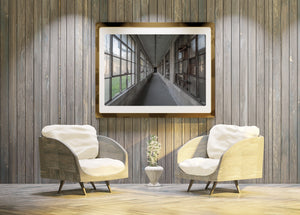 An abandoned hospital corridor with weathered frames and patches of green outside.