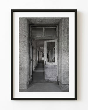 Partly open wooden door and receding corridor at Ellis Island Hospital in black and white.