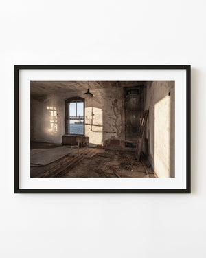 Sunlight enters a decaying Ellis Island Hospital room with the Statue of Liberty visible through its window.