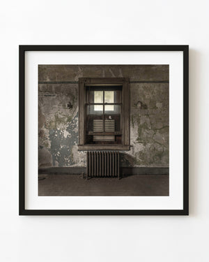 A hospital window and radiator surrounded by peeling grey-green walls on Ellis Island.