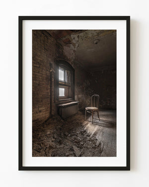An empty chair beside a sunlit window in a decaying Ellis Island staff residence.