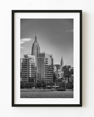 The Empire State and Chrysler buildings rise above Manhattan’s waterfront in black and white.