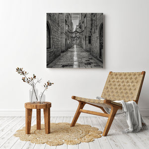 Wooden chair and side table with a decorative rug in a room with a wall art of a narrow alley.