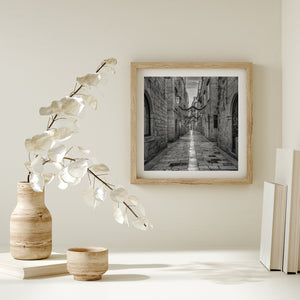 Framed black and white artwork of a narrow street, placed on a shelf with decorative items.