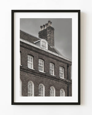 Rows of windows and a tall chimney on an English brick house in black and white.