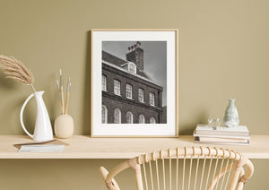 An angled view of brickwork, sash windows and chimney pots in monochrome.