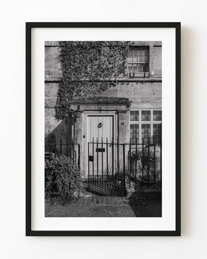 An English front door behind an iron gate, with ivy covering the stone facade, in black and white.