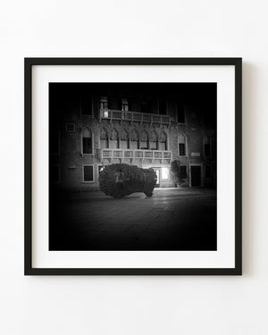 Eros Bendato head sculpture beneath illuminated architecture at night in black and white.