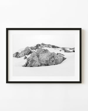 Exposed Antarctic rock rises from a snow-covered landscape in black and white.