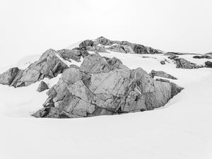 Monochrome Antarctic landscape with fractured rock outcrops surrounded by snow.