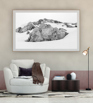 Jagged rock formations break through pale Antarctic snow beneath an open sky.