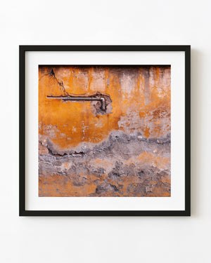 Exposed metal pipe crosses a weathered orange European wall with peeling plaster.