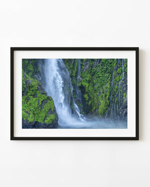 A white waterfall descends between green cliffs in Fiordland National Park, New Zealand.