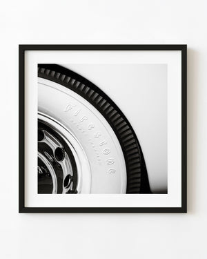 Black and white close-up of a Firestone whitewall tire and reflective chrome wheel.