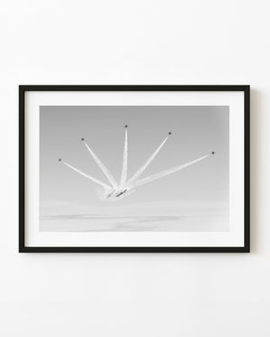 Five aerobatic aircraft fan outward with bright smoke trails across a pale sky in black and white.