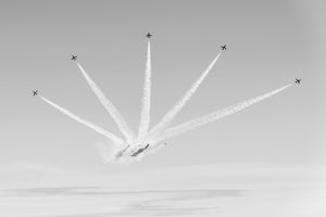 Small aircraft spread across the sky along radiating smoke trails in monochrome.