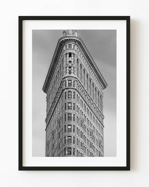 Black and white upward view of New York’s Flatiron Building, showing its curved corner and ornate stone facade.