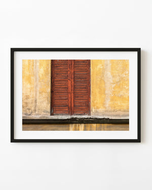 Weathered reddish-brown wooden shutters on a yellow plaster wall in Florence, photographed in colour.