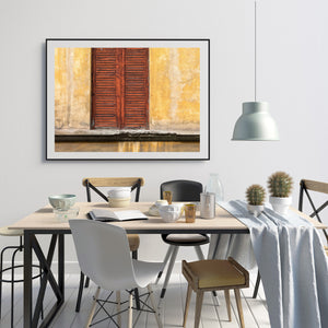 Worn red-brown shutters contrast with mottled yellow and cream plaster.