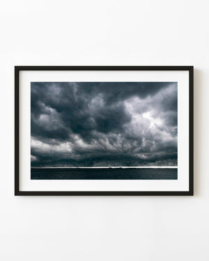 Dark storm clouds gather over the Florida coast above blue-grey water and a thin bright horizon.