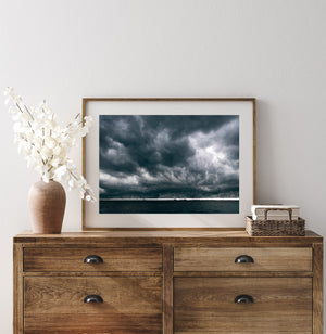 Dense rain clouds fill the sky above dark coastal water in a colour photograph.