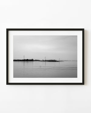 Utility poles and sagging wires cross still Florida Gulf Coast water, with reflections, in black and white.