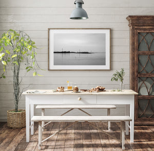 Low islands and a distant tree-lined shore stretch across a pale black and white seascape.