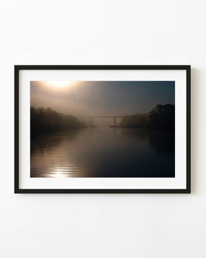 Morning sun glows through mist above Florida’s Intracoastal Waterway, with a distant bridge and dark wooded banks.